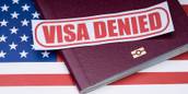 the words &quot;VISA DENIED&quot; in red letters on a white background, on top of a burgundy leather book that is placed on a U.S. flag.