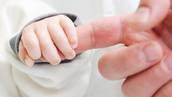 A baby holds onto her parent's index finger. 